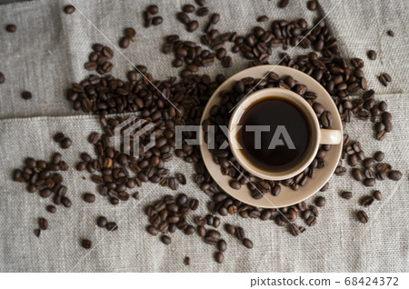 Coffee cup with roasted coffee beans on linen background. Mug of black coffe with scattered coffee beans. Fresh coffee beans. Coffee cup with roasted coffee beans on linen background. Mug of black coffe with scattered coffee beans. Fresh coffee beans. 68424372
