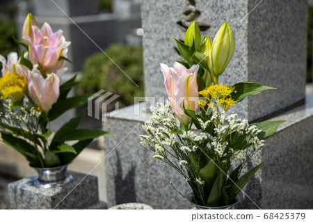 A grave with pink, yellow and white flowers 68425379
