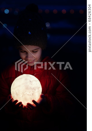 teenager girl in cap and jacket holds a full moon 68426304