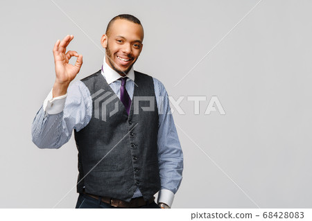 Happy african-american businessman showing ok sign with smile over grey background Happy african-american businessman showing ok sign with smile over grey background 68428083