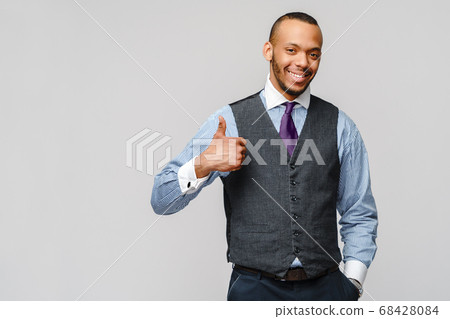 Happy african-american businessman showing his thumb up with smile over grey background Happy african-american businessman showing his thumb up with smile over grey background 68428084