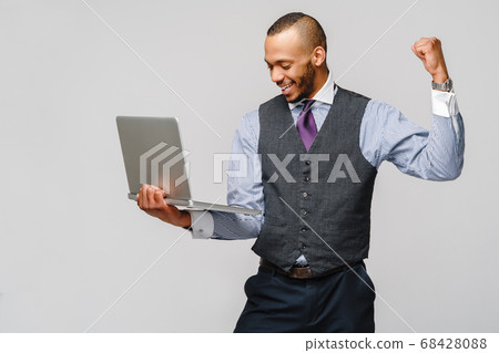 Young smart shouting african-american businessman doing success win gesture and holding laptop pc Young smart shouting african-american businessman doing success win gesture and holding laptop pc 68428088