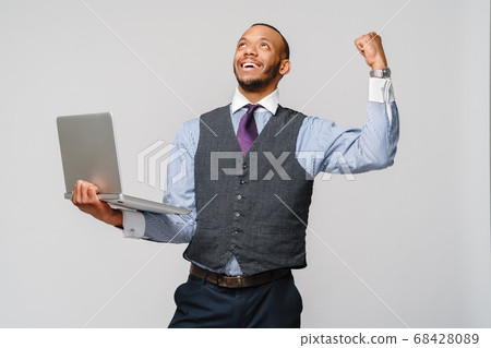 Young smart shouting african-american businessman doing success win gesture and holding laptop pc Young smart shouting african-american businessman doing success win gesture and holding laptop pc 68428089