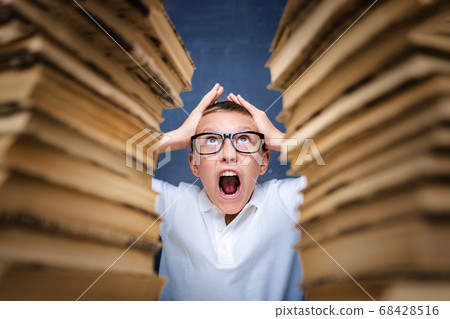 Young boy in stress getting crazy while studying and doing homework in children education concept sitting between two piles of books. Young boy in stress getting crazy while studying and doing homework in children education concept sitting between two piles of books. 68428516