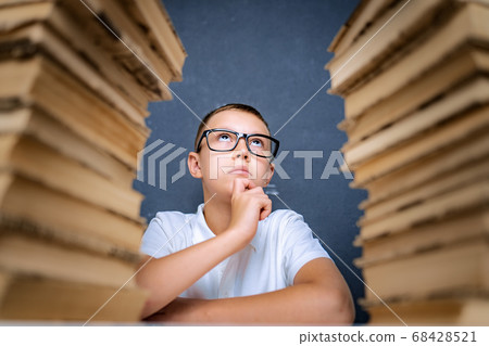 Smart boy in glasses sitting between two piles of books and look up thoughtfully Smart boy in glasses sitting between two piles of books and look up thoughtfully 68428521