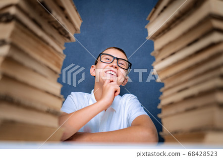 Happy smart boy in glasses sitting between two piles of books and look up smiling Happy smart boy in glasses sitting between two piles of books and look up smiling 68428523