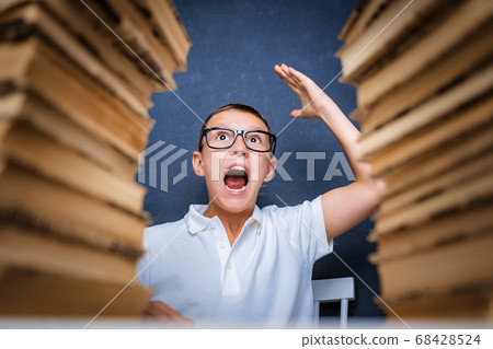 Happy smart boy in glasses sitting between two piles of books and look up smiling Happy smart boy in glasses sitting between two piles of books and look up smiling 68428524