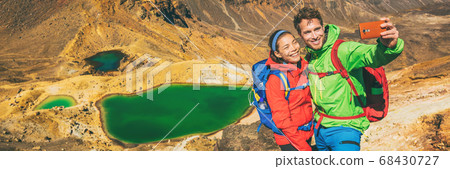 New Zealand Tongariro Alpine Crossing Hiking tourists couple selfie at Emerald Lakes. Happy backpackers tramping taking phone photo of themselves at volcanic mountains. Tramping track of New Zealand 68430727