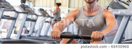 Man training on rowing machine in fitness gym 68430968