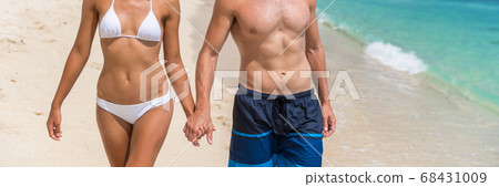 Body care sexy people in swimwear on beach banner background. Couple holding hands, woman in bikini, man in swim trunks showing toned abs stomach for healthy fitness concept Body care sexy people in swimwear on beach banner background. Couple holding hands, woman in bikini, man in swim trunks showing toned abs stomach for healthy fitness concept 68431009