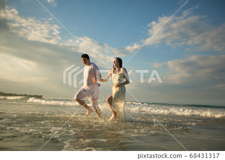 couple in white running forward in water on beach. 68431317