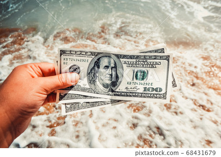 Girl holding a money bill of 300 dollars on background of sea waves Girl holding a money bill of 300 dollars on background of sea waves 68431679