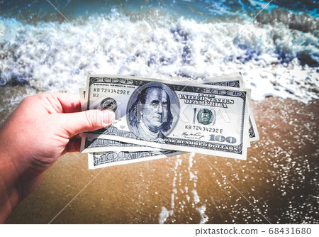 Girl holding a money bill of 300 dollars on background of sea waves Girl holding a money bill of 300 dollars on background of sea waves 68431680