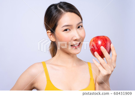 A sporty Asian woman in sportswear holding an apple isolated on white background 68431909