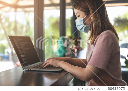 Asian woman wearing protective mask working on laptop in coffee shop 68432075