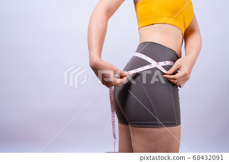 Asian sporty woman measuring her waist by measure tape isolated on white background Asian sporty woman measuring her waist by measure tape isolated on white background 68432091