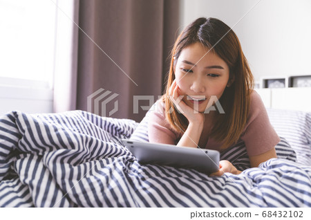 Young asian woman using tablet on bed browsing item to buy and pay with credit card 68432102