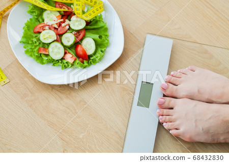 Diet concept, woman measures weight on electronic scales and diet salad with yellow measuring tape 68432830