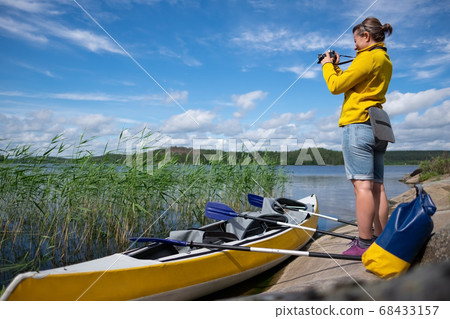 woman resting by the lake after kayaking making photos on her camera. woman resting by the lake after kayaking making photos on her camera. 68433157