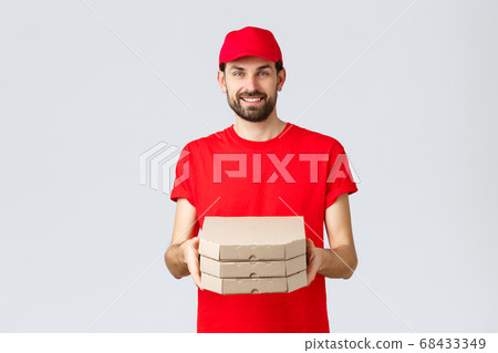 Food delivery, quarantine, stay home and order online concept. Smiling nice bearded courier in red uniform cap and t-shirt, handing clients boxes with pizza, deliver order, grey background Food delivery, quarantine, stay home and order online concept. Smiling nice bearded courier in red uniform cap and t-shirt, handing clients boxes with pizza, deliver order, grey background 68433349