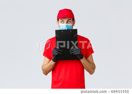 Packages, delivery, covid-19 quarantine, transfer orders. Curious and excited courier in red uniform, gloves and face medical mask, look away scheming, holding clipboard with order form 68433350