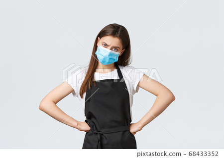Covid-19 social distancing, cafe employees, coffee shops and coronavirus concept. Dissatisfied serious-looking frowning store manager in black apron and medical mask frowning and looking frustrated Covid-19 social distancing, cafe employees, coffee shops and coronavirus concept. Dissatisfied serious-looking frowning store manager in black apron and medical mask frowning and looking frustrated 68433352