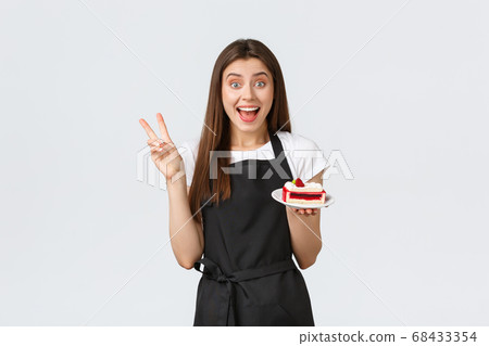 Grocery store employees, small business and coffee shops concept. Excited cheerful female cafe worker in black apron smiling amused and showing peace gesture as serving delicious cake in cafe Grocery store employees, small business and coffee shops concept. Excited cheerful female cafe worker in black apron smiling amused and showing peace gesture as serving delicious cake in cafe 68433354