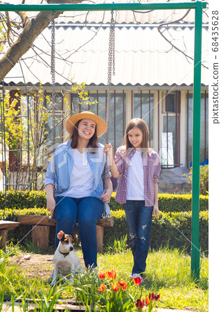 mom and daughter with dog on swing in garden mom and daughter with dog on swing in garden 68435628