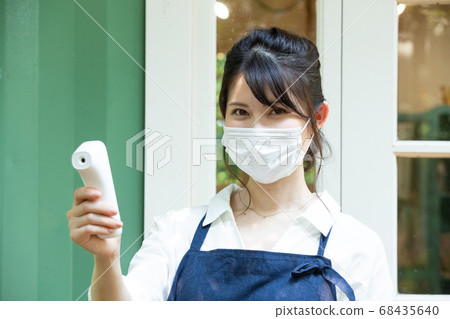 A woman in an apron with a non-contact thermometer 68435640
