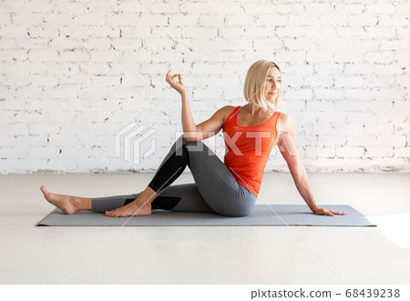 Attractive caucasian woman practice hatha yoga indoor in loft white studio. Seated side twist pose, selective focus. Attractive caucasian woman practice hatha yoga indoor in loft white studio. Seated side twist pose, selective focus. 68439238