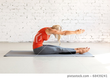 Attractive caucasian woman practice pilates. Seated forward fold on a mat, in loft white studio. Indoor workout, selective focus. Attractive caucasian woman practice pilates. Seated forward fold on a mat, in loft white studio. Indoor workout, selective focus. 68439241