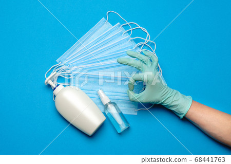 Human hand in protective glove, face protective masks and hand sanitizer or liquid soap isolated over blue background 68441763