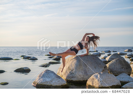 Slim woman doing Wild Thing pose on stone Slim woman doing Wild Thing pose on stone 68447028
