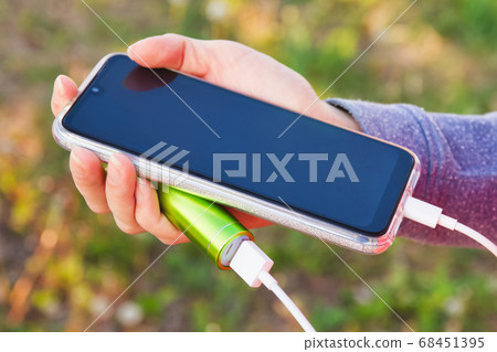A girl uses a smartphone outdoors while charging A girl uses a smartphone outdoors while charging 68451395