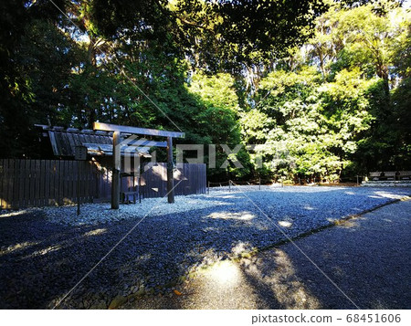 Sunbeams and blue shadows in the forest illuminating an old wooden torii gate and a small wooden shrine beyond the gravel 68451606