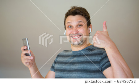 the happy guy inserts a wireless headset into his ear. Man and modern technologies. listen to music. finger pointing the happy guy inserts a wireless headset into his ear. Man and modern technologies. listen to music. finger pointing 68456758
