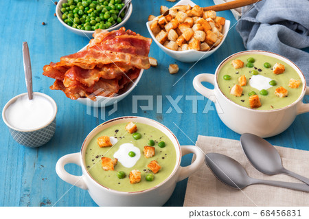 Homemade creamy grean pea soup with slices of grilled bacon and roasted rusks, blue background. Homemade creamy grean pea soup with slices of grilled bacon and roasted rusks, blue background. 68456831