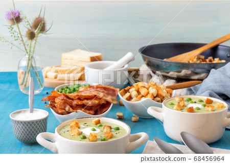 Homemade creamy grean pea soup with slices of grilled bacon and roasted rusks, blue background. 68456964
