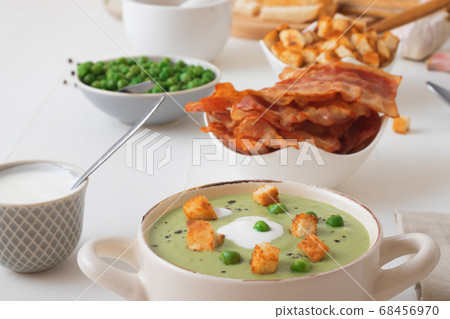 Homemade creamy grean pea soup with slices of grilled bacon and roasted rusks, white background. 68456970