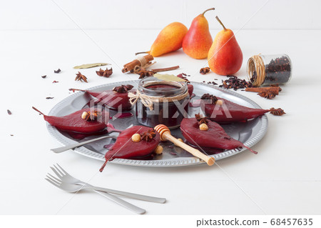Poached pears with hibiscus syrup, sweet fruit dessert with hazelnuts and anise stars spice. White wooden table.  68457635