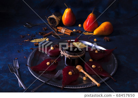 Poached pears with hibiscus syrup, sweet fruit dessert with hazelnuts and anise stars spice. Dark wooden table.  68457650