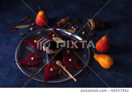 Poached pears with hibiscus syrup, sweet fruit dessert with hazelnuts and anise stars spice. Dark blue wooden table.  68457842