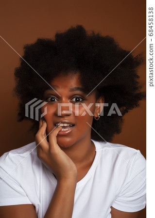 pretty young african american woman with curly hair posing cheerful gesturing on brown background, lifestyle people concept 68458138