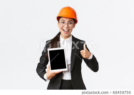 Impressed young female realtor, estate agent showing building during construction, wear safety helmet and business suit, holding digital tablet and make thumbs-up, recommend purchase Impressed young female realtor, estate agent showing building during construction, wear safety helmet and business suit, holding digital tablet and make thumbs-up, recommend purchase 68459750