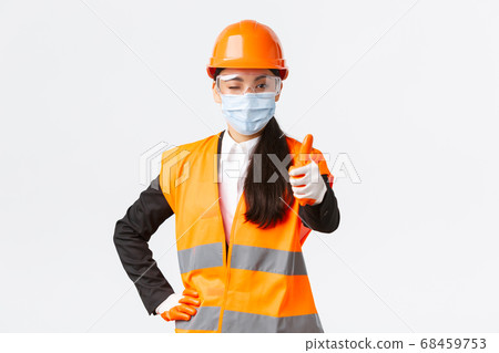 Covid-19 safety protocol at enterpise, construction and preventing virus concept. Confident asian female engineer, architect in face mask and helmet showing thumb-up, guarantee quality of building Covid-19 safety protocol at enterpise, construction and preventing virus concept. Confident asian female engineer, architect in face mask and helmet showing thumb-up, guarantee quality of building 68459753