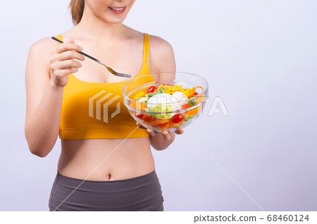 A sporty Asian woman in sportswear eating salad isolated on white background A sporty Asian woman in sportswear eating salad isolated on white background 68460124