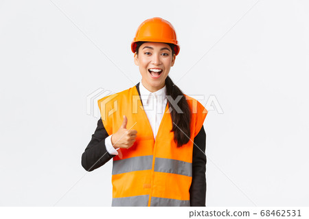 Supportive and pleased happy asian female chief engineer in safety helmet showing thumbs-up in approval, satisfied with construction work. Industrial woman in reflecive jacket inspect area 68462531