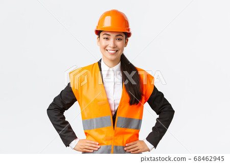 Successful young female asian businesswoman, architect in safety helmet, reflective jacket, standing confident and determined, smiling assured, building houses, posing over white background 68462945