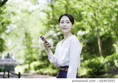 看智能手機的少婦反對新鮮的綠樹 看智能手機的少婦反對新鮮的綠樹 68463091
