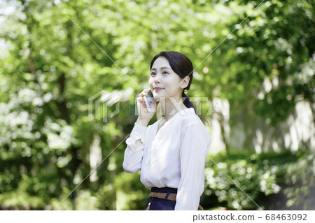 看智能手機的少婦反對新鮮的綠樹 看智能手機的少婦反對新鮮的綠樹 68463092